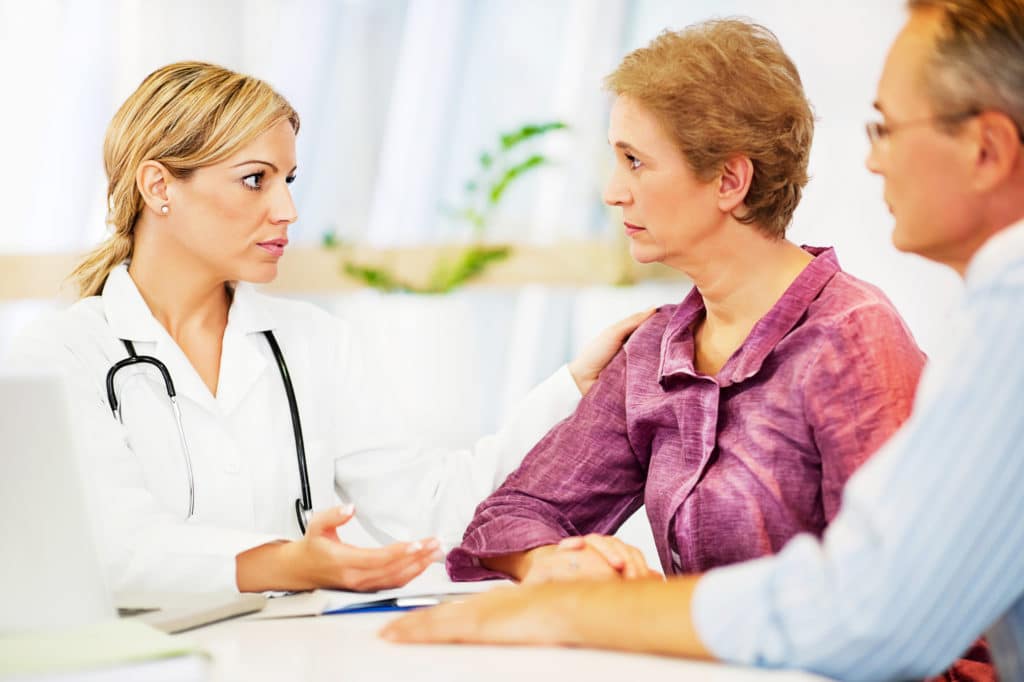Serious mature couple talking with female doctor in a Doctor's Office.  Doctor giving support mature woman.