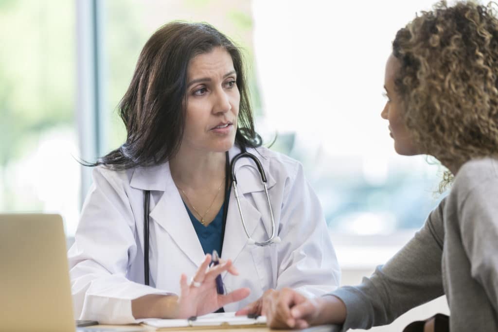 Worried female doctor gestures while discussing something serious with young woman.