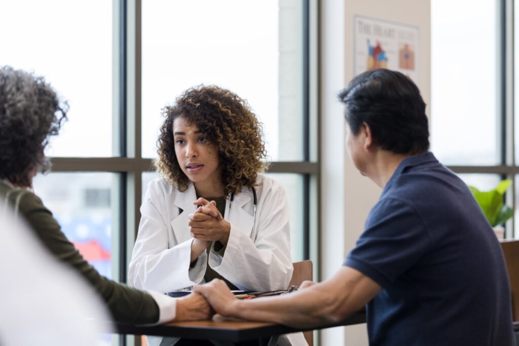 Doctor has serious look while talking to couple The doctor has a serious look while talking to the mature adult couple holding hands.